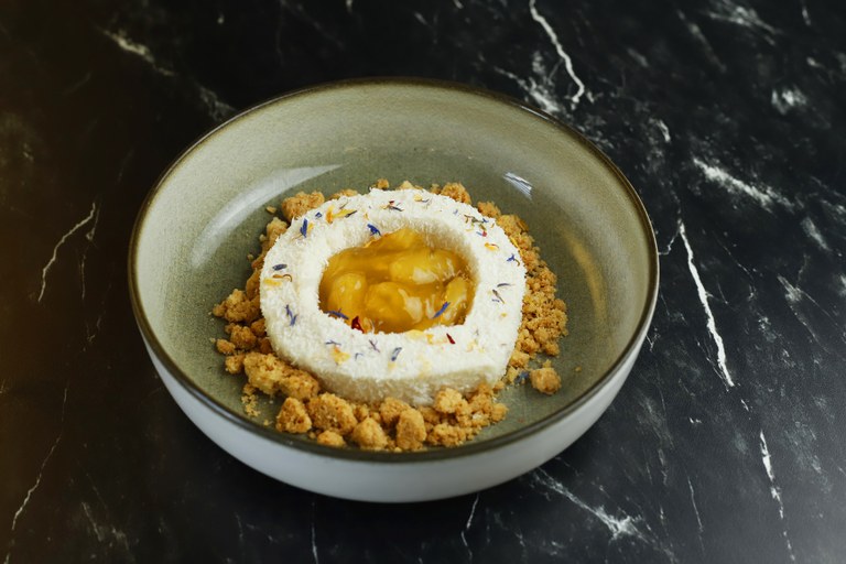 Round shaped pannacotta with mango fruitful in the middle and sprinkled with coconut