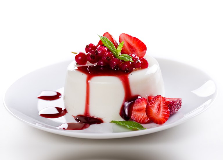 Panna cotta with strawberry sauce and fresh strawberries on the side, on white background